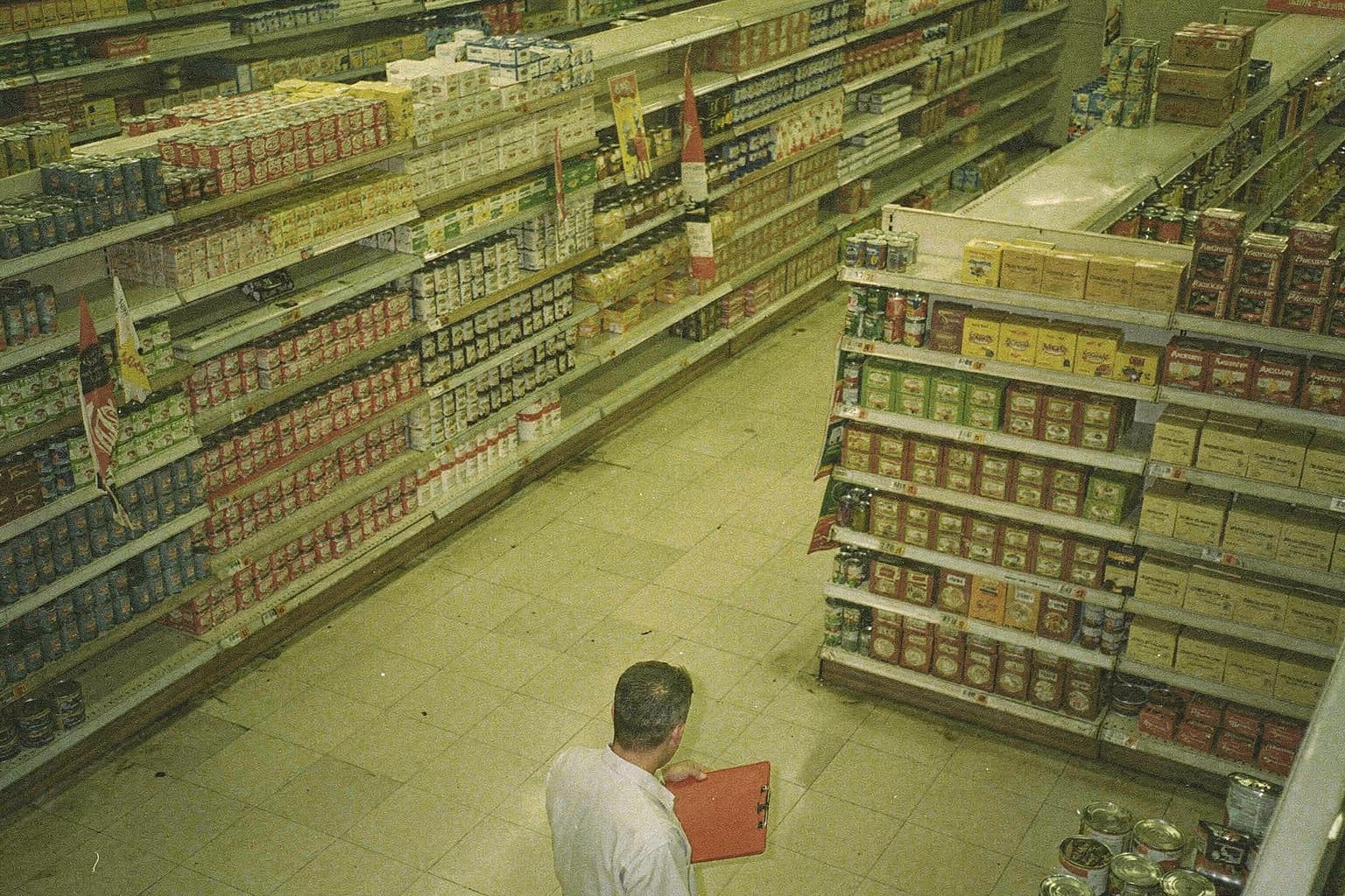 A merchandiser with a red clipboard inspecting many parallel grocery-store aisles